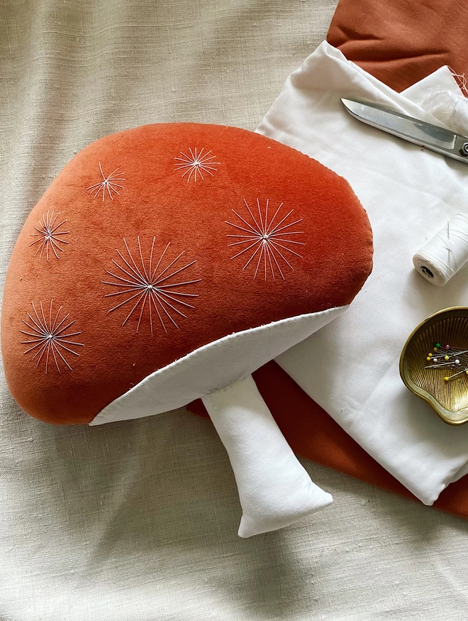 Rust coloured mushroom cushion with sewing paraphernalia 