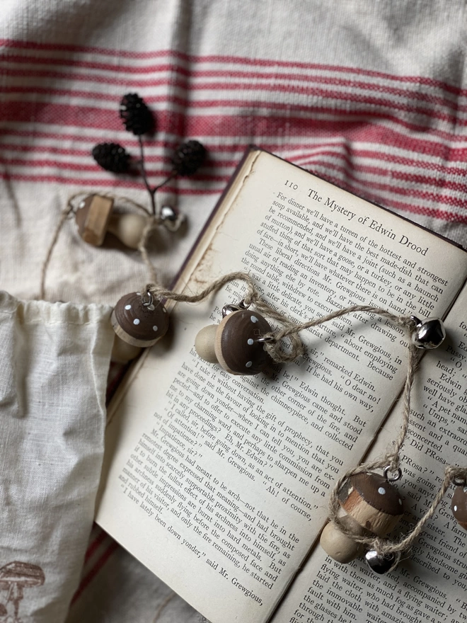 A string of Hand Painted Wooden Toadstool Bell Garlands trailing across an opened book atop a red and white striped cloth