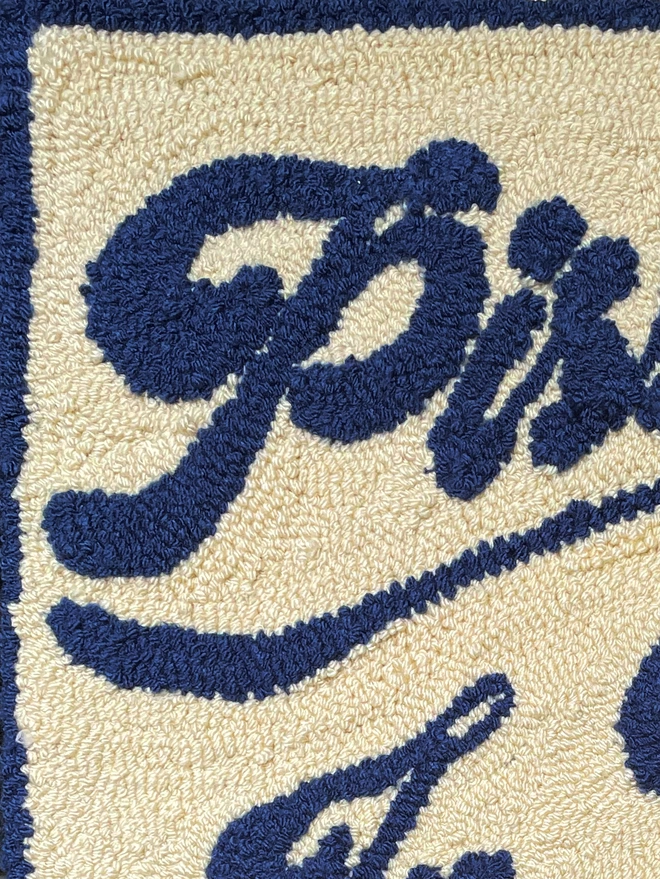 Close up of blue wool script lettering on a cream tufted background
