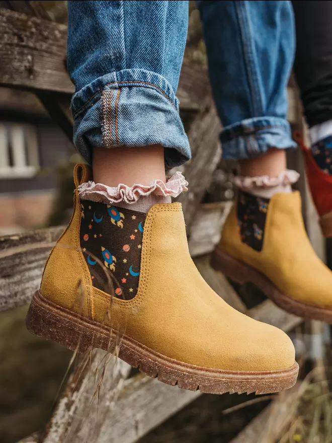 Child Wearing Mustard/ yellow coloured suede chelea boots with a space ship print
