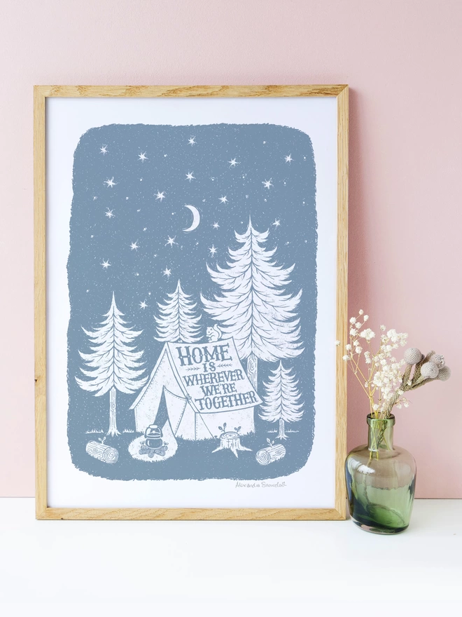 home is wherever we're together print in grey and white in a wood frame with green vase of flowers