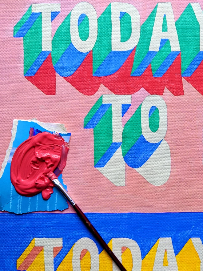 Detail of a painting showing the words ‘Today To’ in 3d typography in green, blue, pink and yellow by artist Survival Techniques. A paintbrush rests on the canvas with a small palette of wet pink paint.