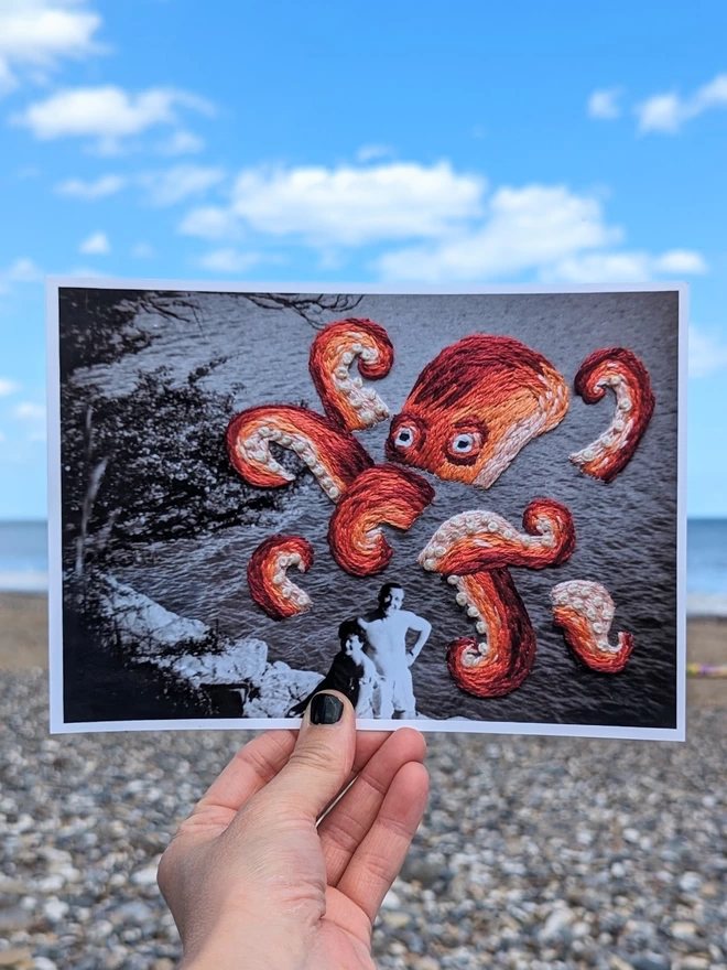 B&W print of couple with orange embroidered octopus behind them, held against beach background 
