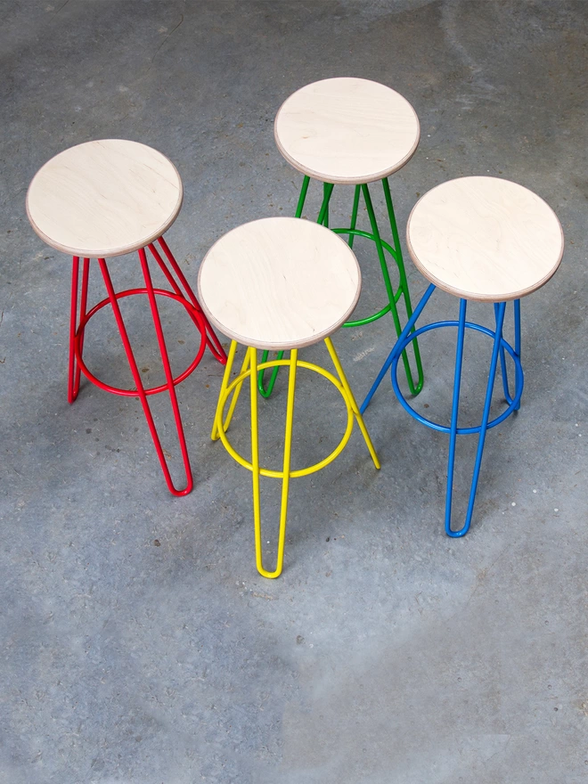 set of four hairpin leg bar stools with plywood seats and different brightly coloured legs - one red, one yellow, one green and one blue