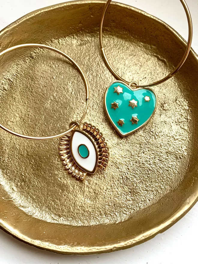 Large gold hoop earrings on gold dish with turquoise heart and turquoise evil eye charms