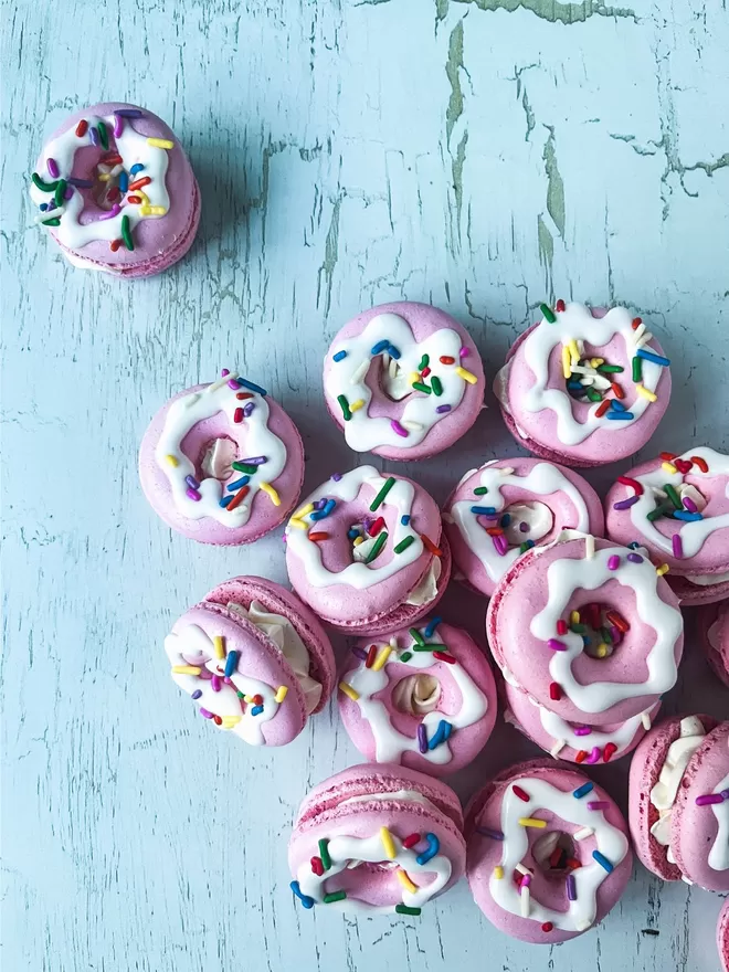 a pile of pink donuts with vibrant & colourful sprinkles on top in a pile against a white background