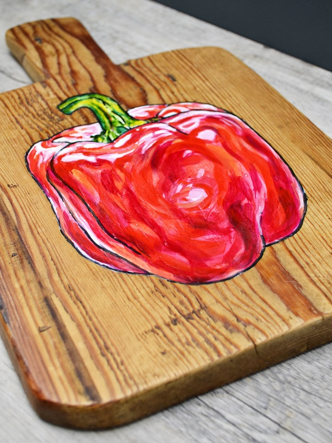 Close up of a wooden chopping board with handpainted design of a red pepper