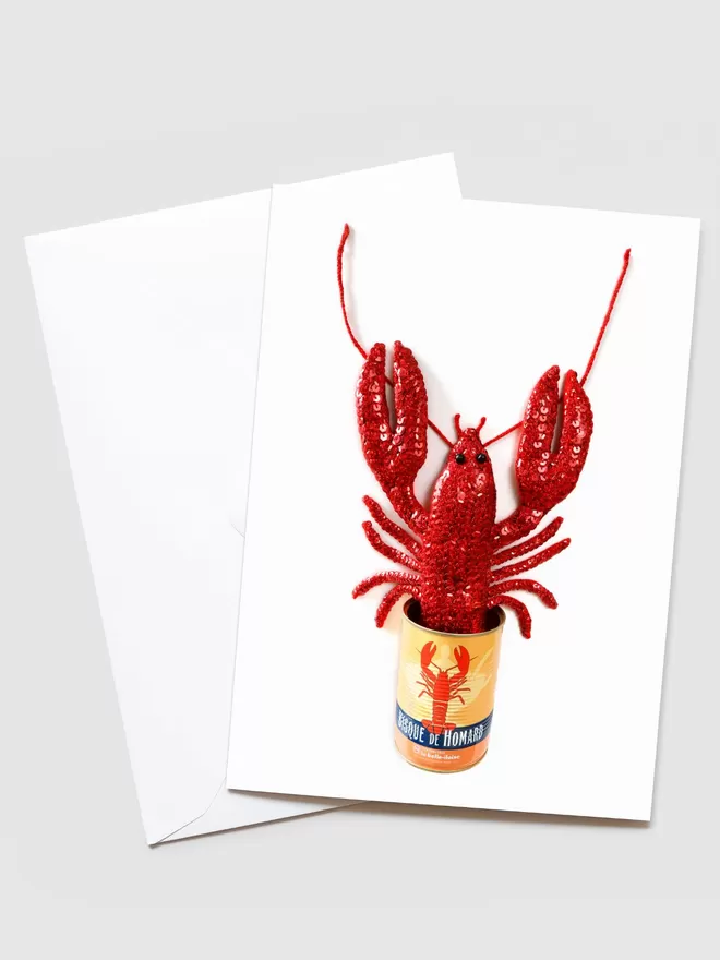 Kate Jenkins Lobster Bisque In A Can Card seen with a blank envelope behind. On the card is Kate's handmade sequin lobster in a tin can.