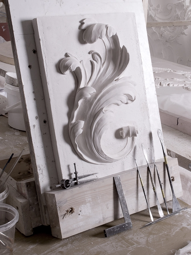 Plaster bas-relief wall plaque with acanthus leaf design on an easel with tools underneath