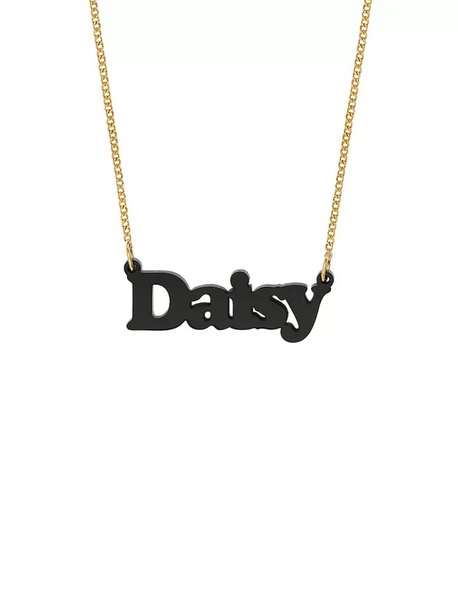 Personalised Name Neckace from Tatty Devine. The Necklace is the word Daisy laser cut from Recycled Black Acrylic on a gold-plated chain.