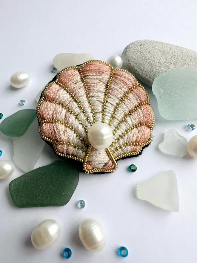 Clam shell brooch with pearl centre with sea glass pearls and sequins in the background 