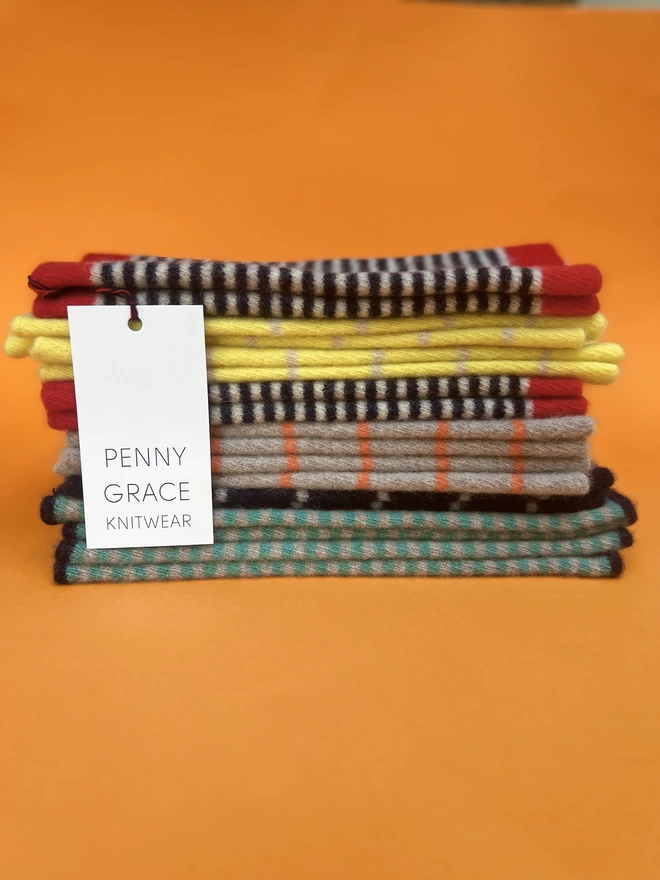 A stack of knitted multi coloured wristwarmers on an orange background