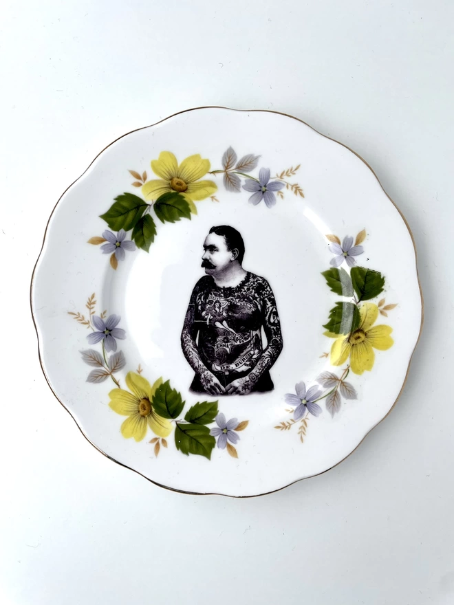 vintage plate with an ornate border, with a printed vintage illustration of a Victorian tattooed man in the middle 