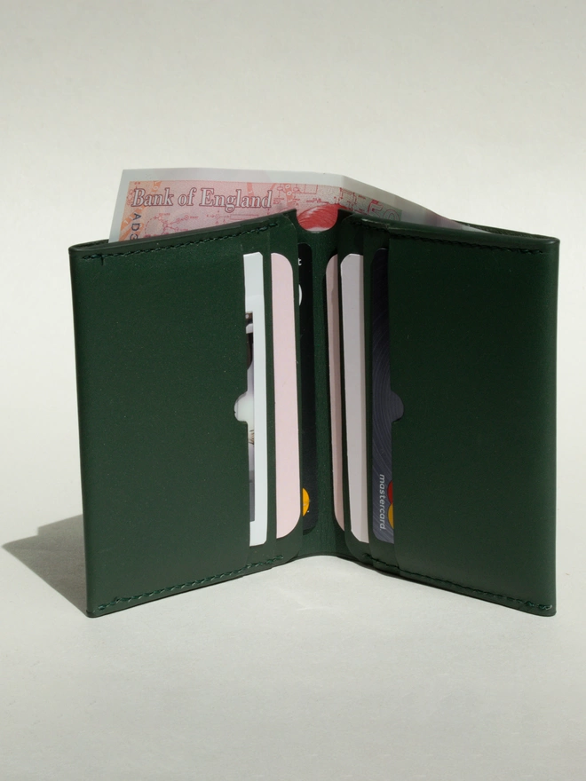 Dark Green Bifold Wallet open with a shadow falling on the left of it. It is filled with cards and a £50 note