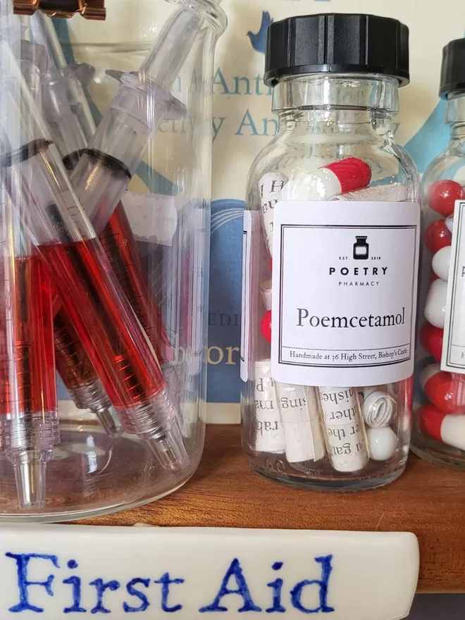 Glass pill bottle containing red and white and clear Poemcetamol poetry pills printed on banana paper- displayed on Poetry Pharmacy shelves