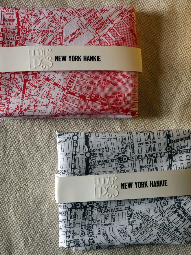 Two folded NYC map hankies, one in red, one in grey