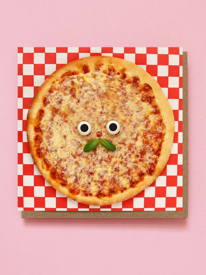A cheesy pizza card with a basil moustache. on a red & white check tablecloth 