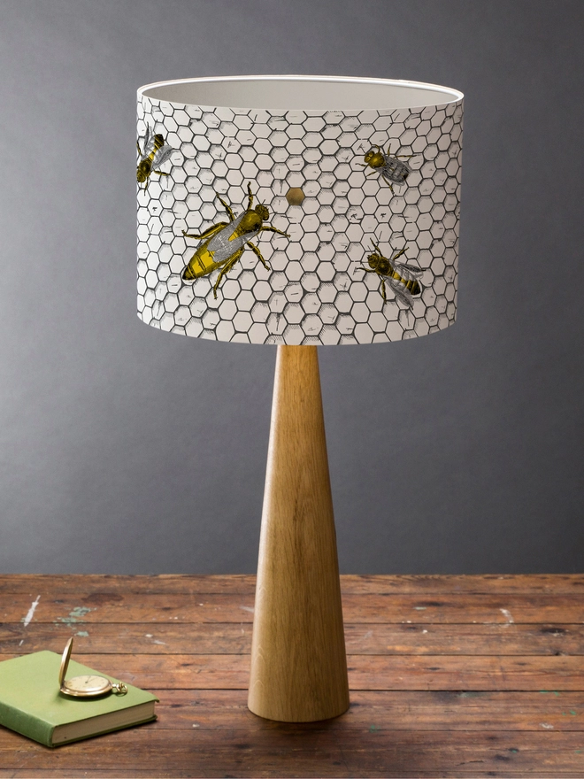 Drum Lampshade featuring honey bees on a honeycomb on a wooden base on a shelf with books and ornaments