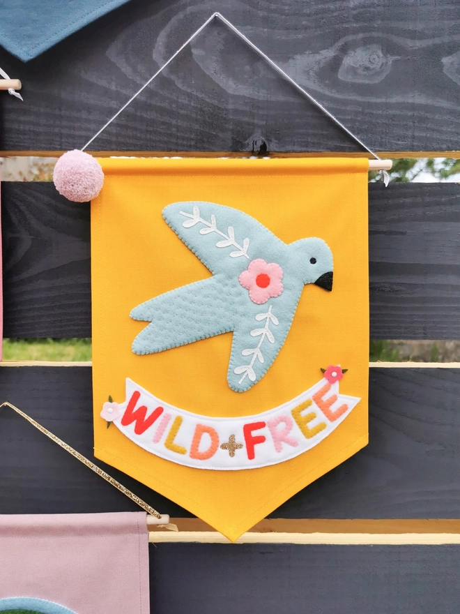 Light mustard wild and free banner with a blue bird hanging on a black wooden fence