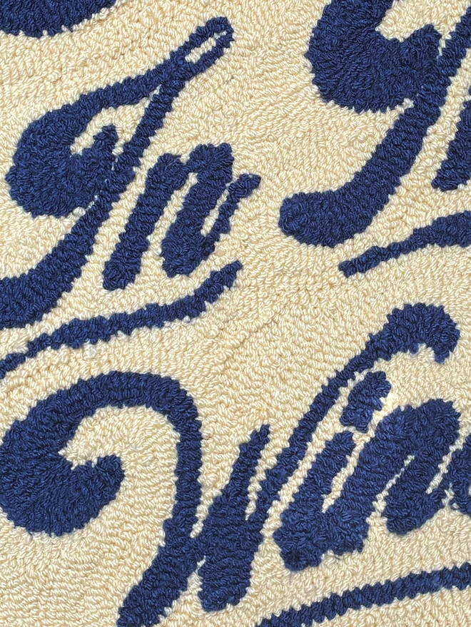 Close up of blue wool script lettering on a cream tufted background