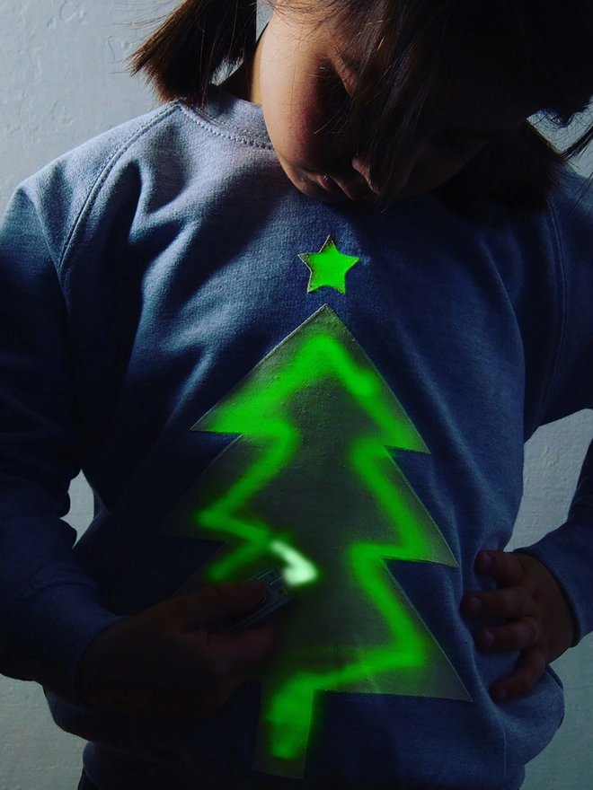 Girl drawing with penlight onto a glow in the dark xmas jumper with tree printed on it