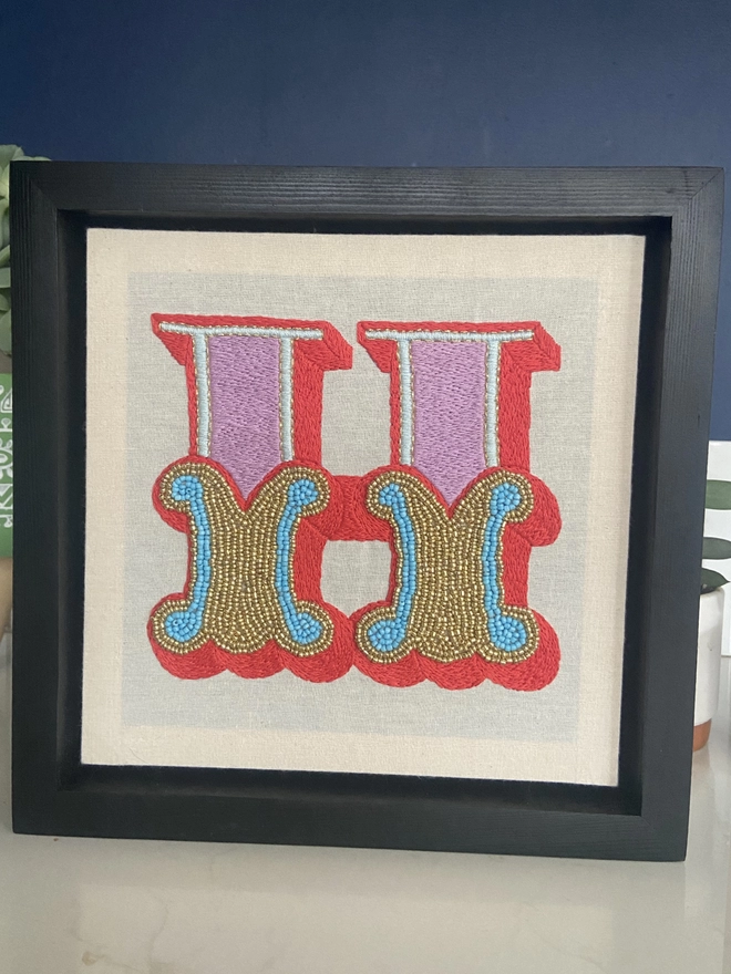 An embroidered letter H in a box frame 
