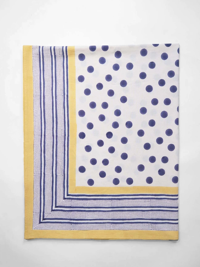 Block printed cream tablecloth featuring a navy spot, navy stripe border and yellow edging, folded in half