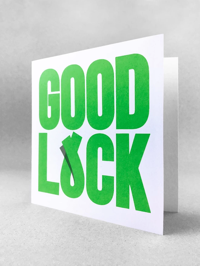  Green bold typography fills the card, ‘GOOD’ on the top, ‘LUCK’ on the bottom - the U has been tweaked to overlap suggesting fingers crossed for luck. there is a small shadow printed to make the overlap clear. This is a studio shot of the card stood slightly open, on a light grey background.