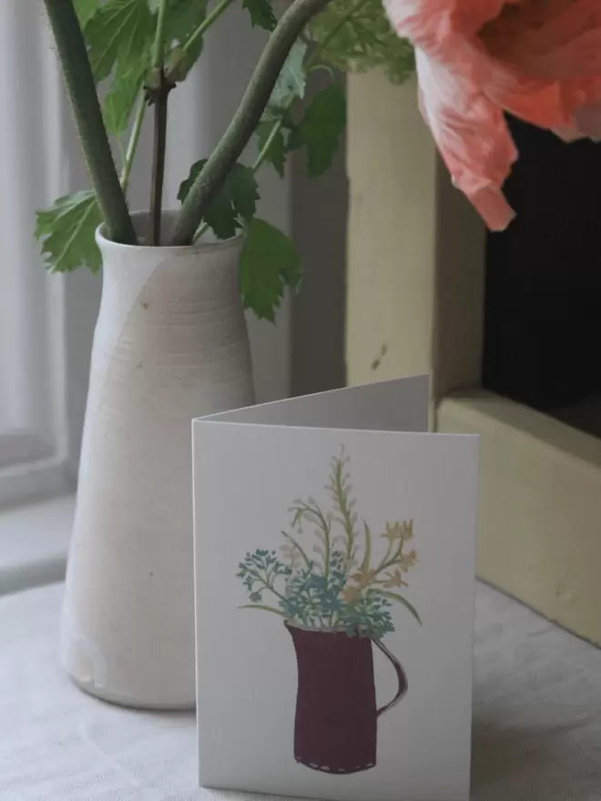 greeting card with flowers in a jug on it, next to a yellow shelf and vase of 