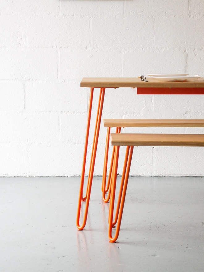 low side on view of a hairpin leg dining set of a table and benches with oak tops and orange hairpin legs