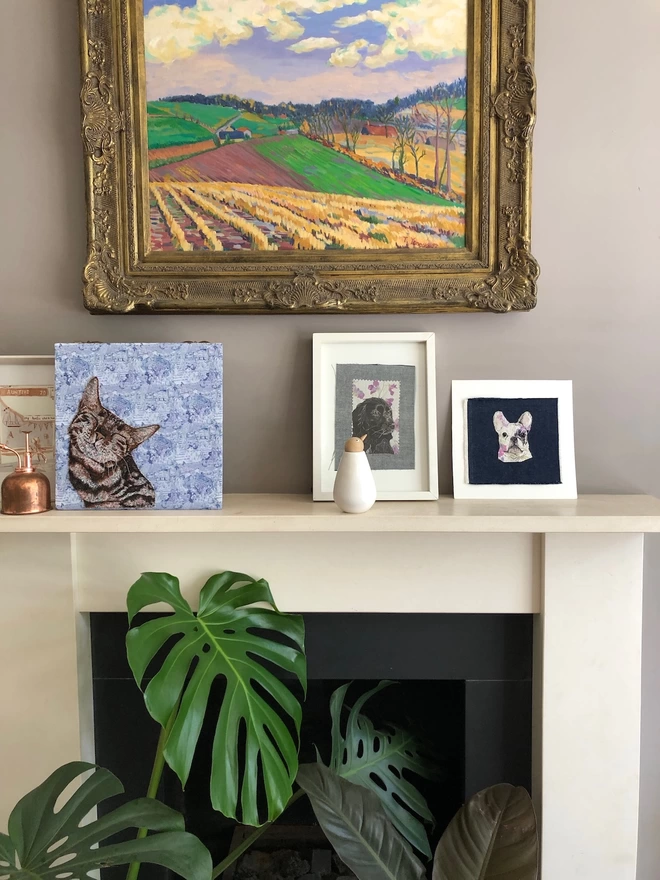 picture of a mantlepiece with three Rocketfullofpie embroidered pet portraits on it