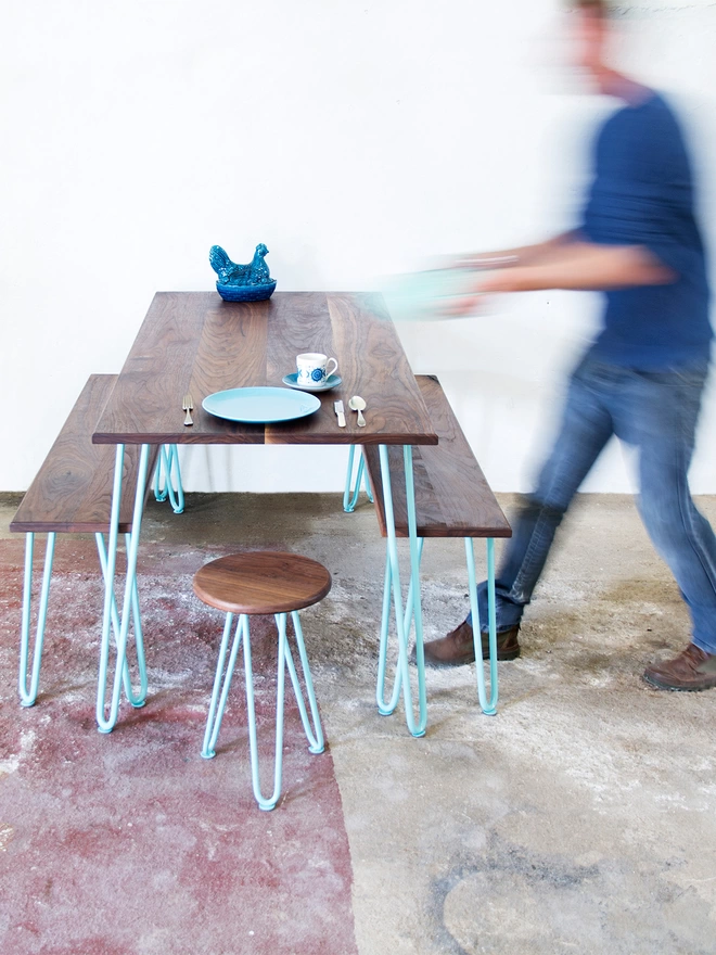 motion blur of a man putting a pot down on a hairpin leg dining table with matching benches either side, with walnut tops and turquoise hairpin legs