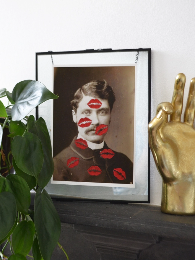 B&W photo print of man covered in embroidered red kisses in frame on mantlepiece
