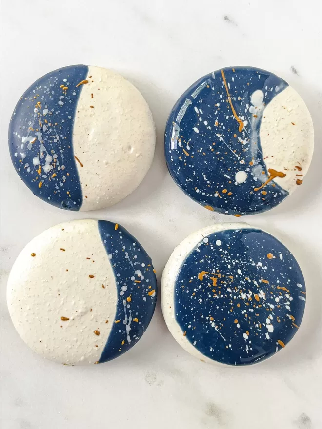 four moon macarons in different moon phases with deep blue starry night with gold & white speckles sitting on top of a marble surface
