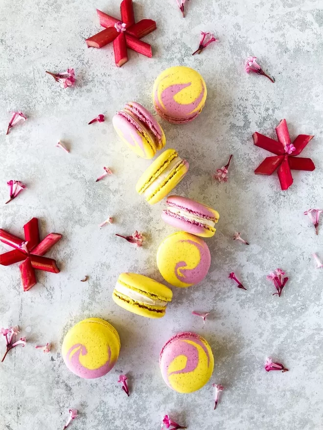 pink and yellow swirl macarons on a table surrounded by flowers & fresh rhubarb