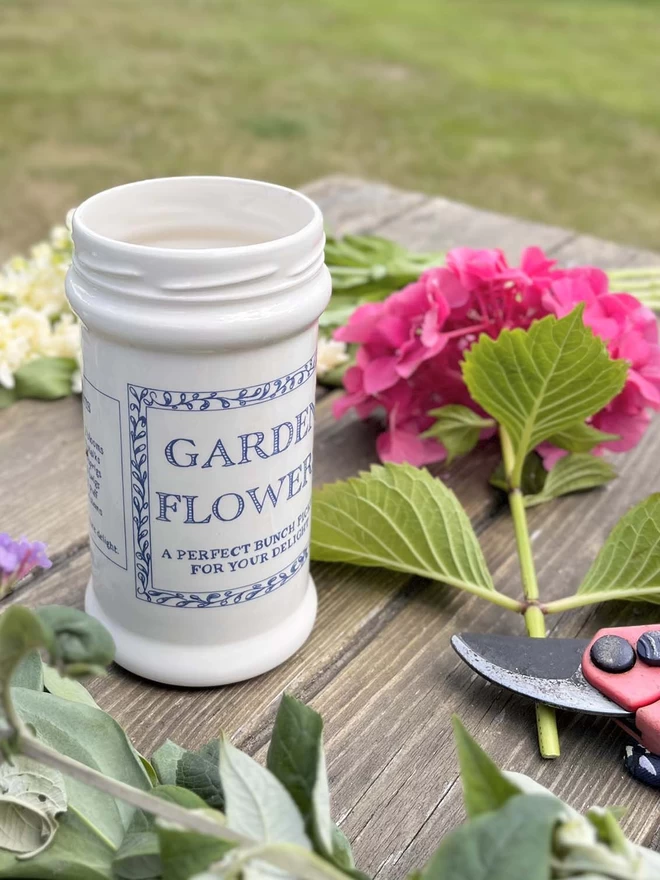 A handmade ceramic jar/vase sits outside amongst freshly cut garden flowers.