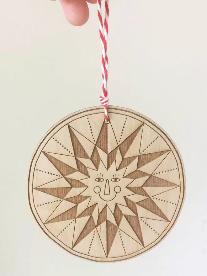 One smiling engraved, wooden star decoration hangs from Fiona's hand on red and white stripy thread