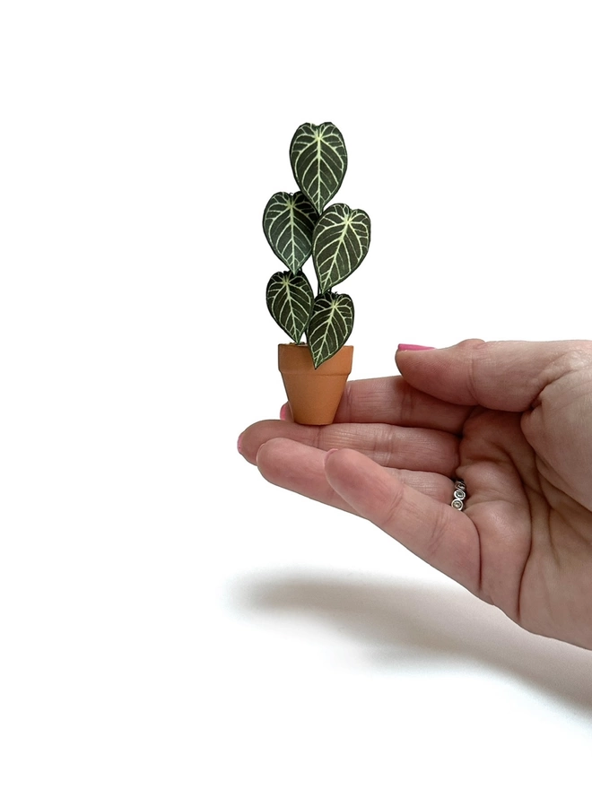 A miniature Anthurium Crystal Hope paper plant ornament balanced on 2 fingers to show the scale of the plant against a white background