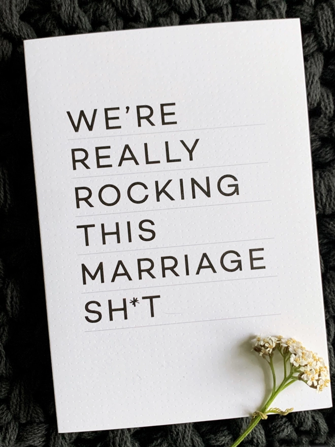Rocking This Marriage Anniversary Card on a dark background that reads "We're really rocking this marriage sh*t" with a flower placed on top.