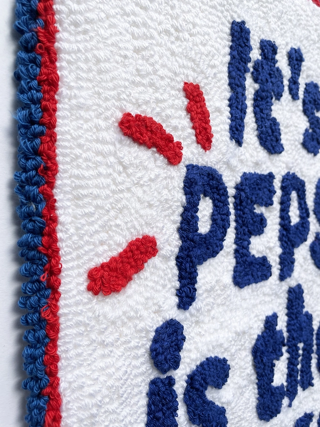 close up of blue tufted "it's Pepsi is that ok?" on a white wool background
