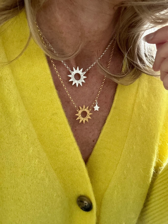 model wearing sterling silver sun charm on sterling silver chain and a gold sun charm on gold chain and silver mini star