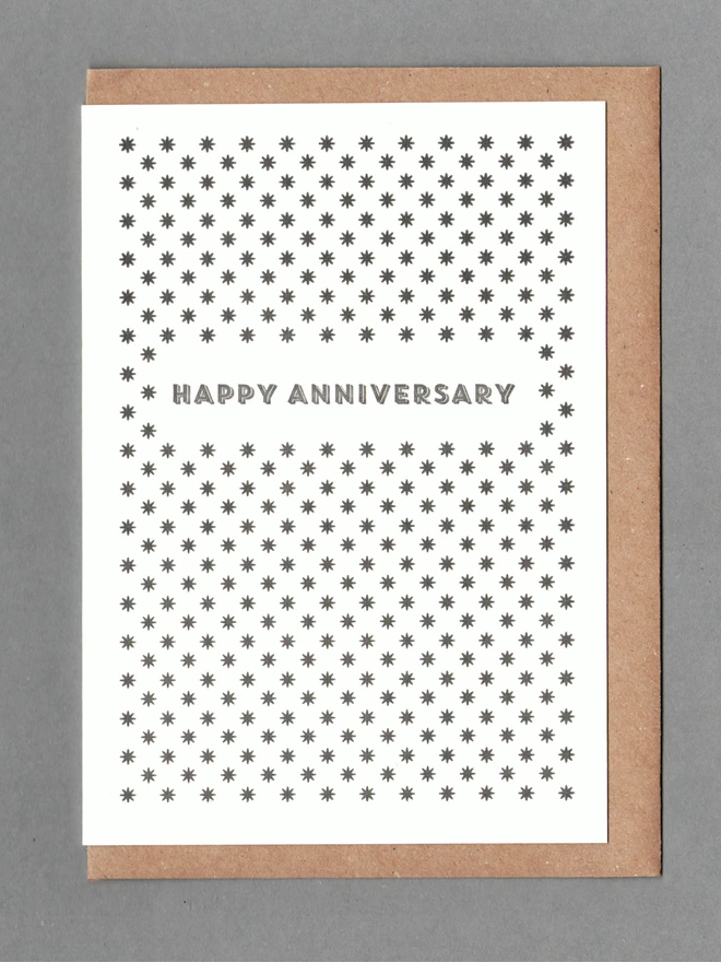 White card with black stars and black text reading 'HAPPY ANNIVERSARY' with a kraft envelope behind it