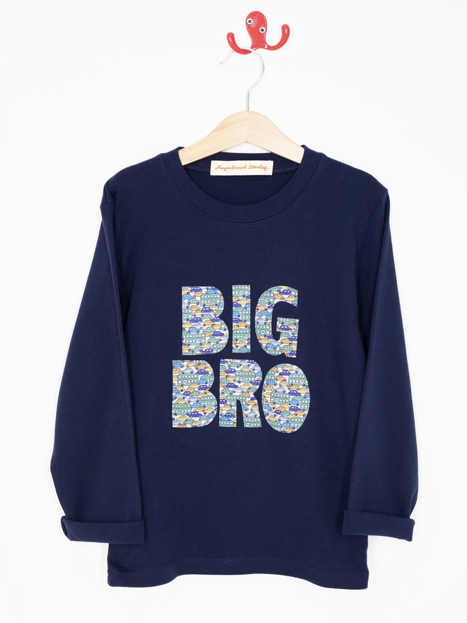 Big Bro appliquéd in a vintage cars Liberty print on a navy cotton long sleeve t-shirt. Hanging on a hanger.