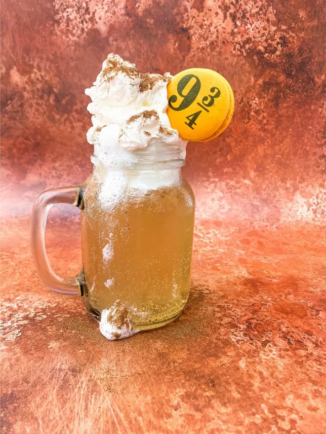 a mason jar filled with lemonade topped with a whipped ice cream and whipped cream and a yellow macaron with 9 3/4 printed on it, all on a copper background