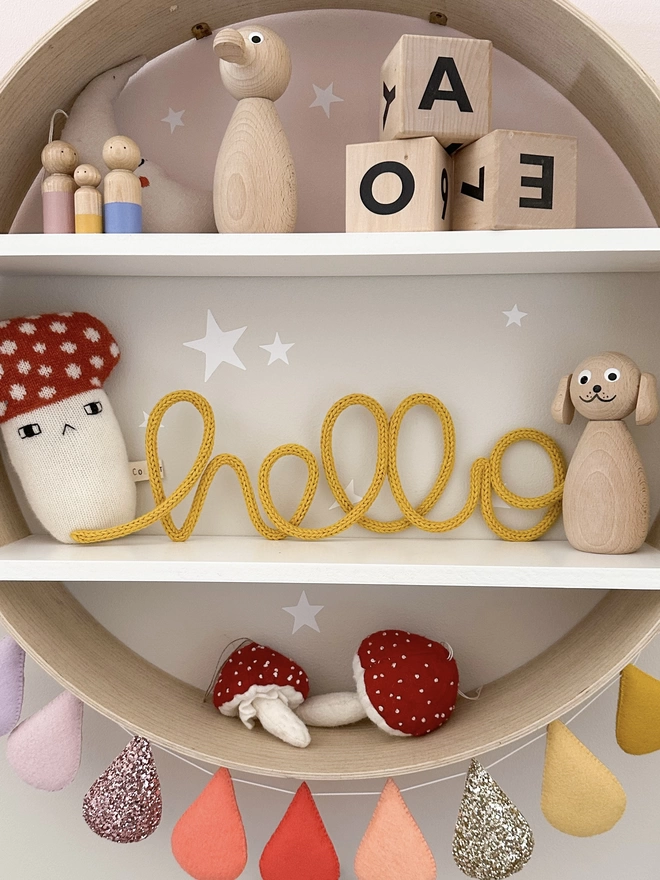 "hello" knitted wall sign baby gift on a shelf in a newborn nursery. 