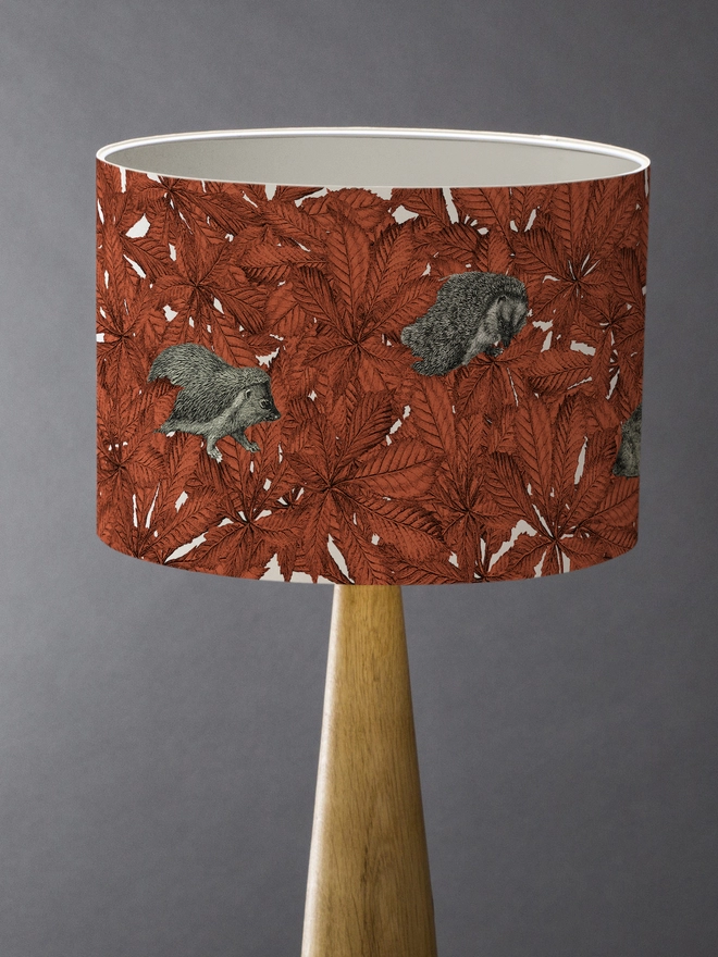 Drum Lampshade featuring hedgehogs in autumnal russet red leaves with a white inner on a wooden base 