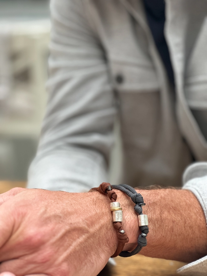 model wears two personalised sterling silver men's bracelets. one on grey cord the other on brown