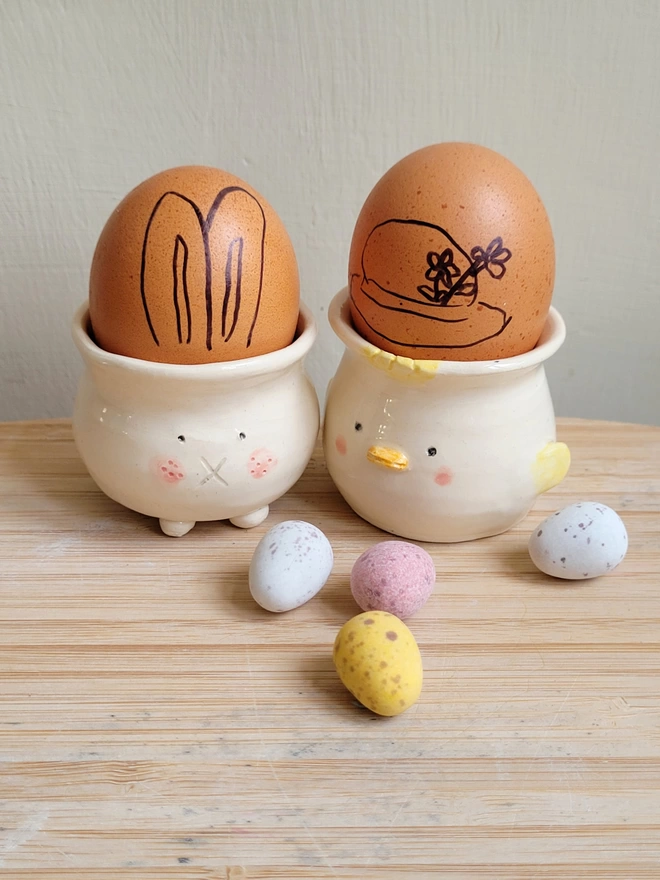 Easter chick and bunny egg cup with brown eggs inside and mini chocolate eggs on the wooden surface in front