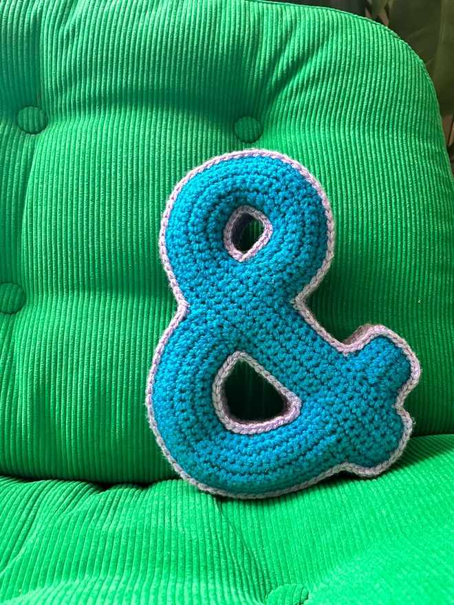 Crochet Cushion shaped like an Ampersand in Blue and Lilac on a green cord chair