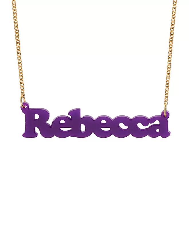 Personalised Name Neckace from Tatty Devine. The Necklace is the word Rebecca laser cut from Purple Acrylic on a gold-plated chain.